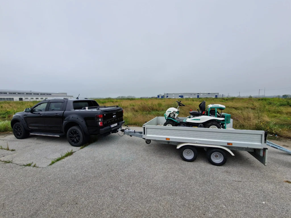 Crni pickup vuče prikolicu s kosilicom